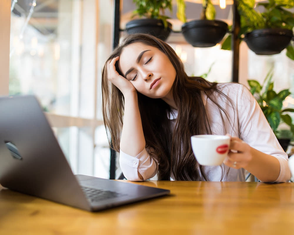 portrait-tired-young-businesswoman-sitting-table-with-laptop-computer-while-holding-cup-coffee-sleeping-cafe1000800 睡眠不足讓您賠上了青春嗎? 長期熬夜老得快!