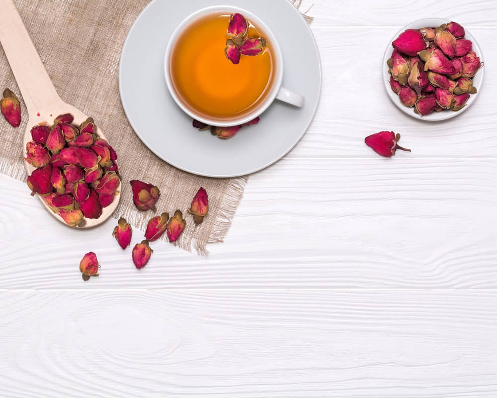 white-cup-with-hot-tea-wooden-spoon-with-dried-flower-buds-linen-napkin1000 玫瑰履歷，玫瑰為何成為愛情的代言人？又為何是女人的不老仙丹？